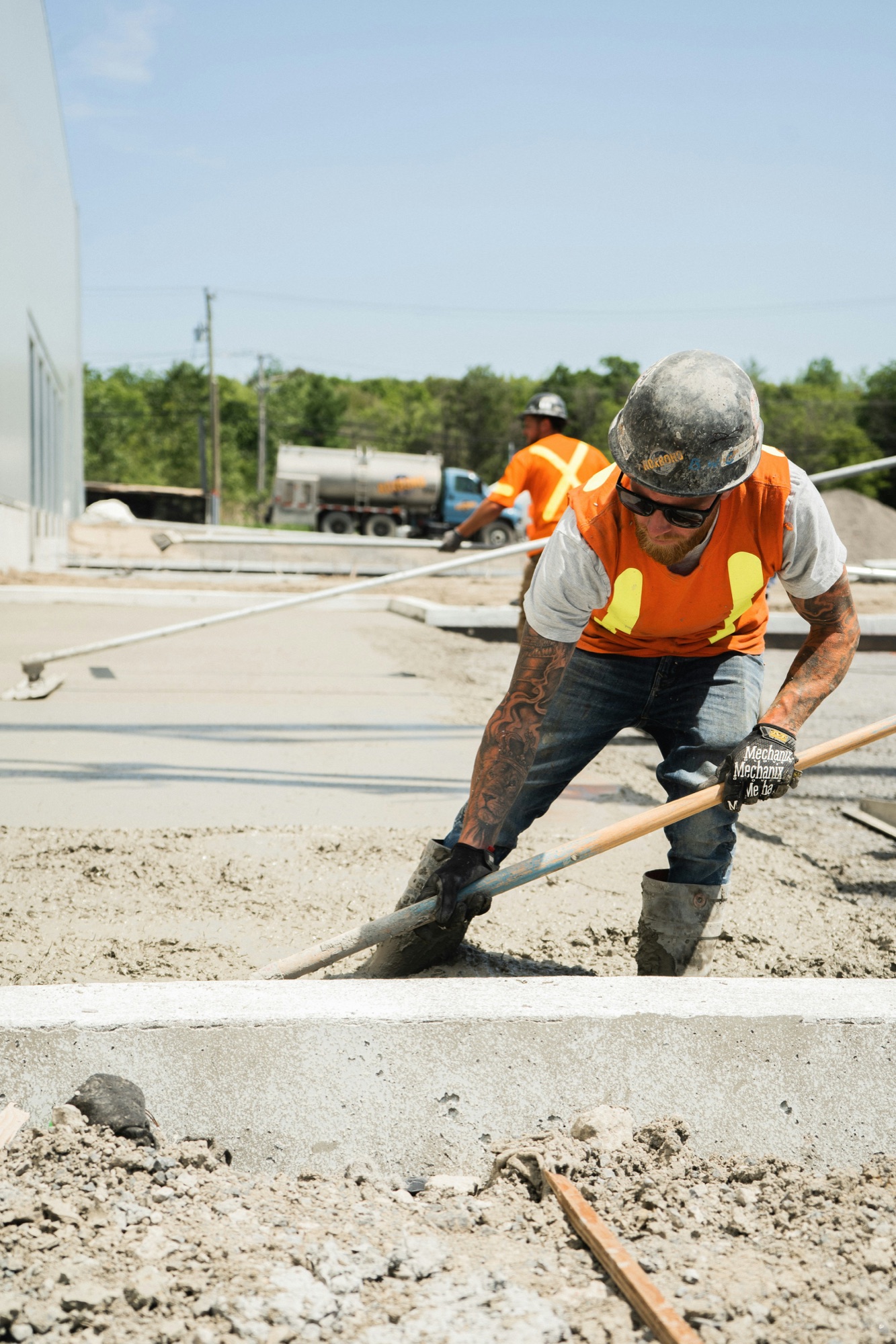 A concrete finisher pulling a straightedge across a fresh slab, with a second worker behind him
