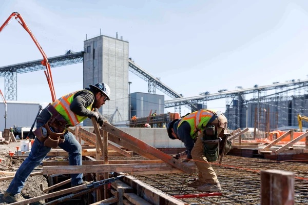 Two carpenters setting wood formwork on a rebar deck at an industrial plant