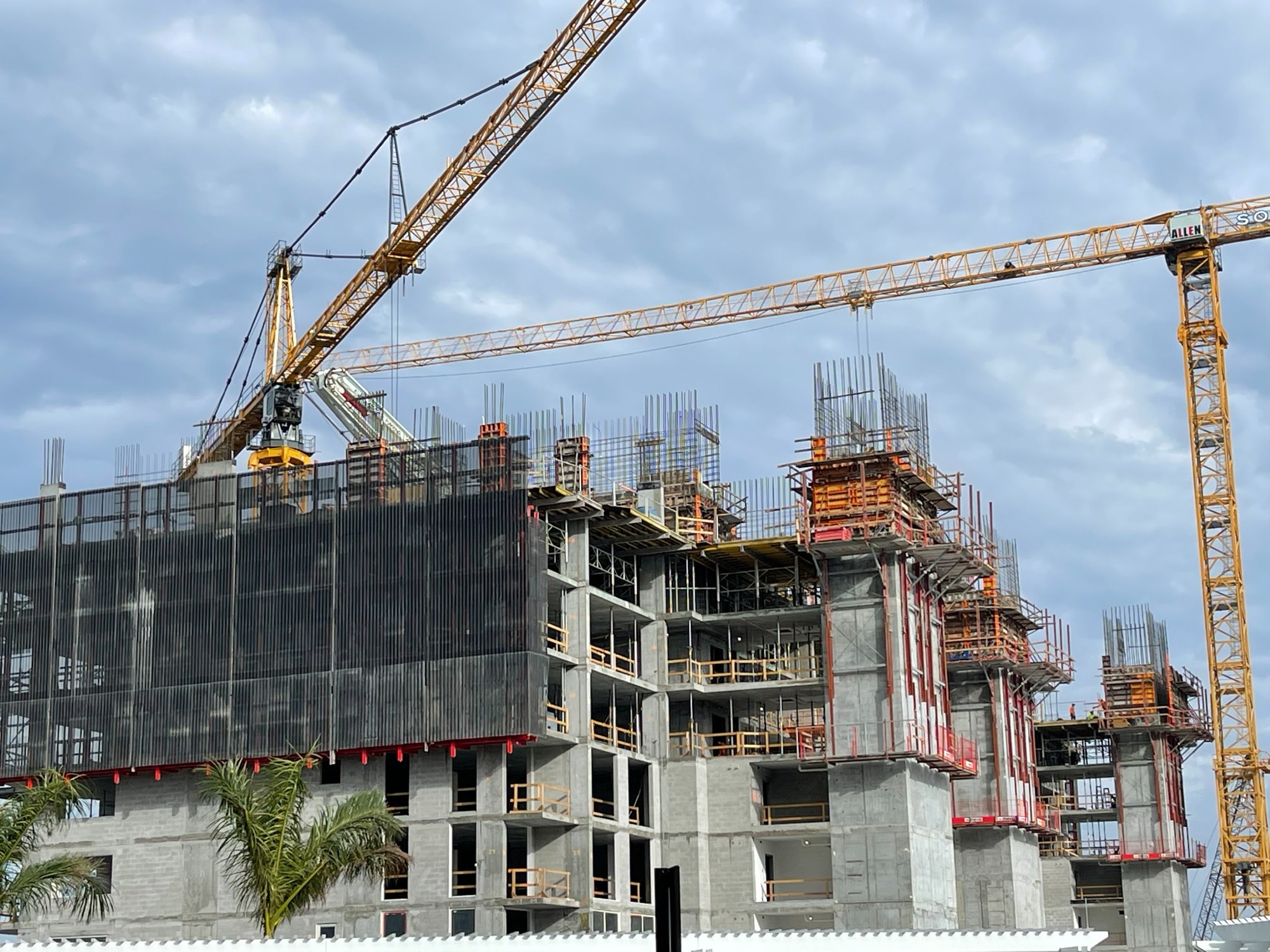 A concrete high-rise under construction between two tower cranes