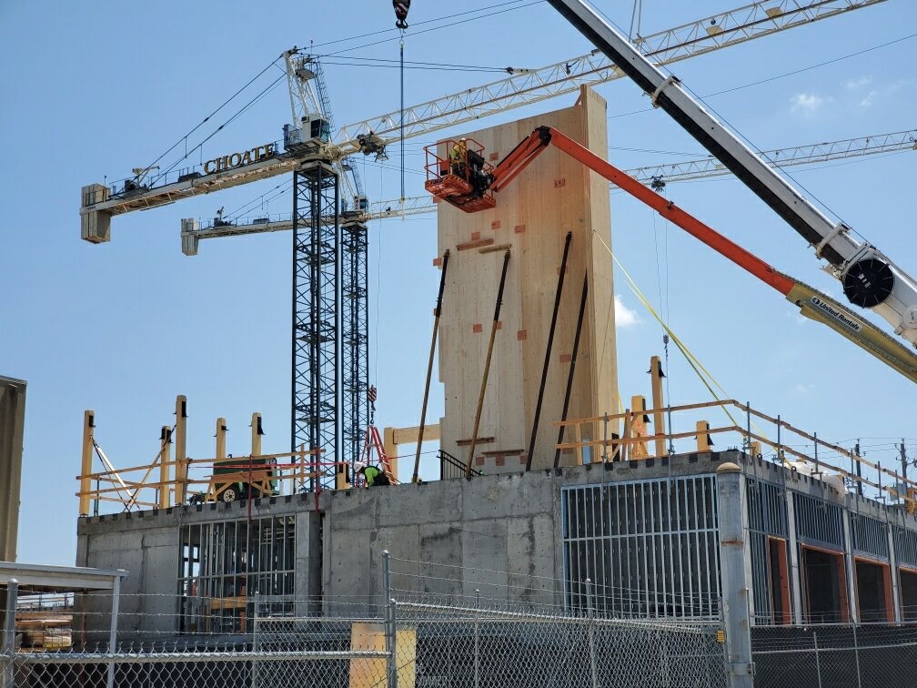 A boom lift and tower cranes raising a tall panel on a concrete building
