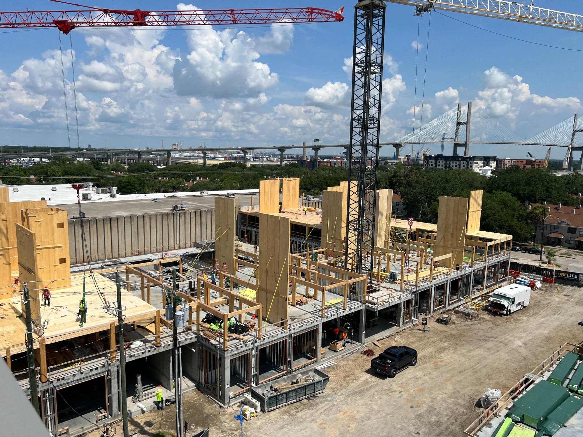 Crews on a multi-story wood and concrete building under construction, with tower cranes