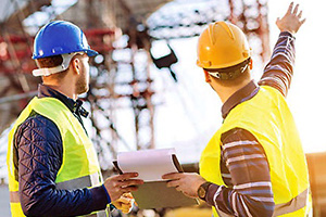 Two supervisors in hard hats reviewing papers on a jobsite