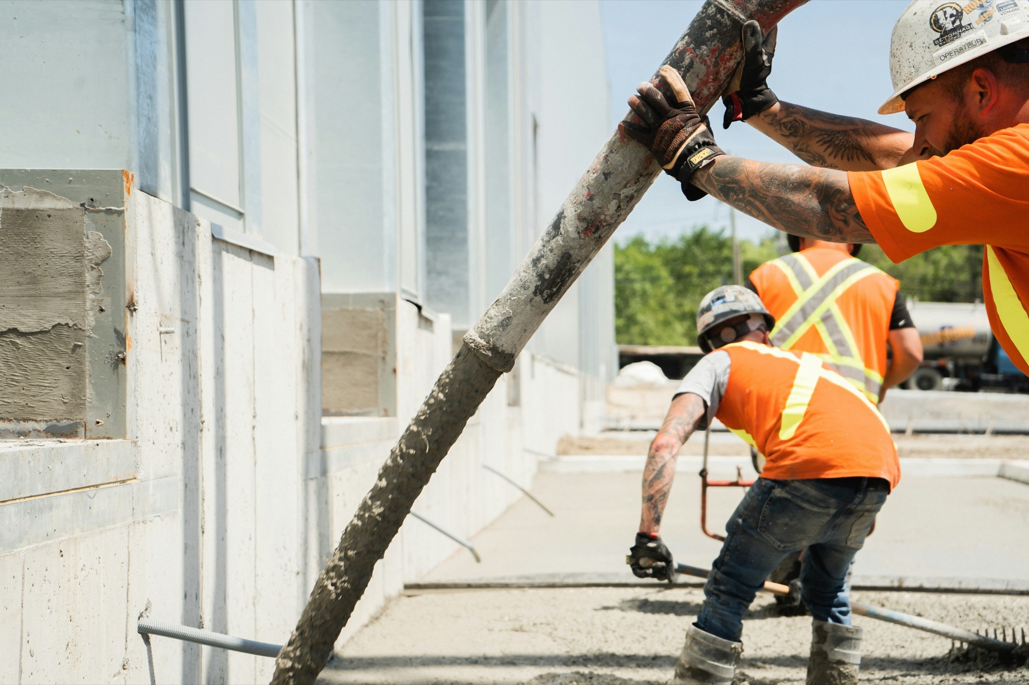 Workers guiding a concrete pump hose along a foundation wall