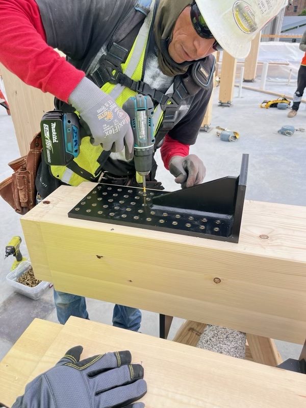 A carpenter driving screws into a steel connector on a timber beam
