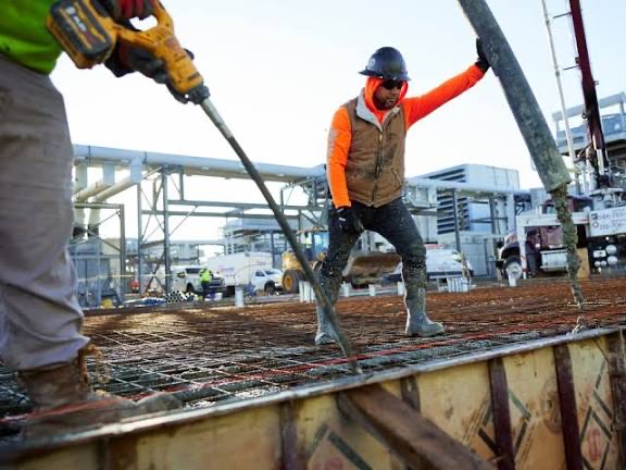 Workers placing a concrete pump hose across a rebar deck at an industrial plant