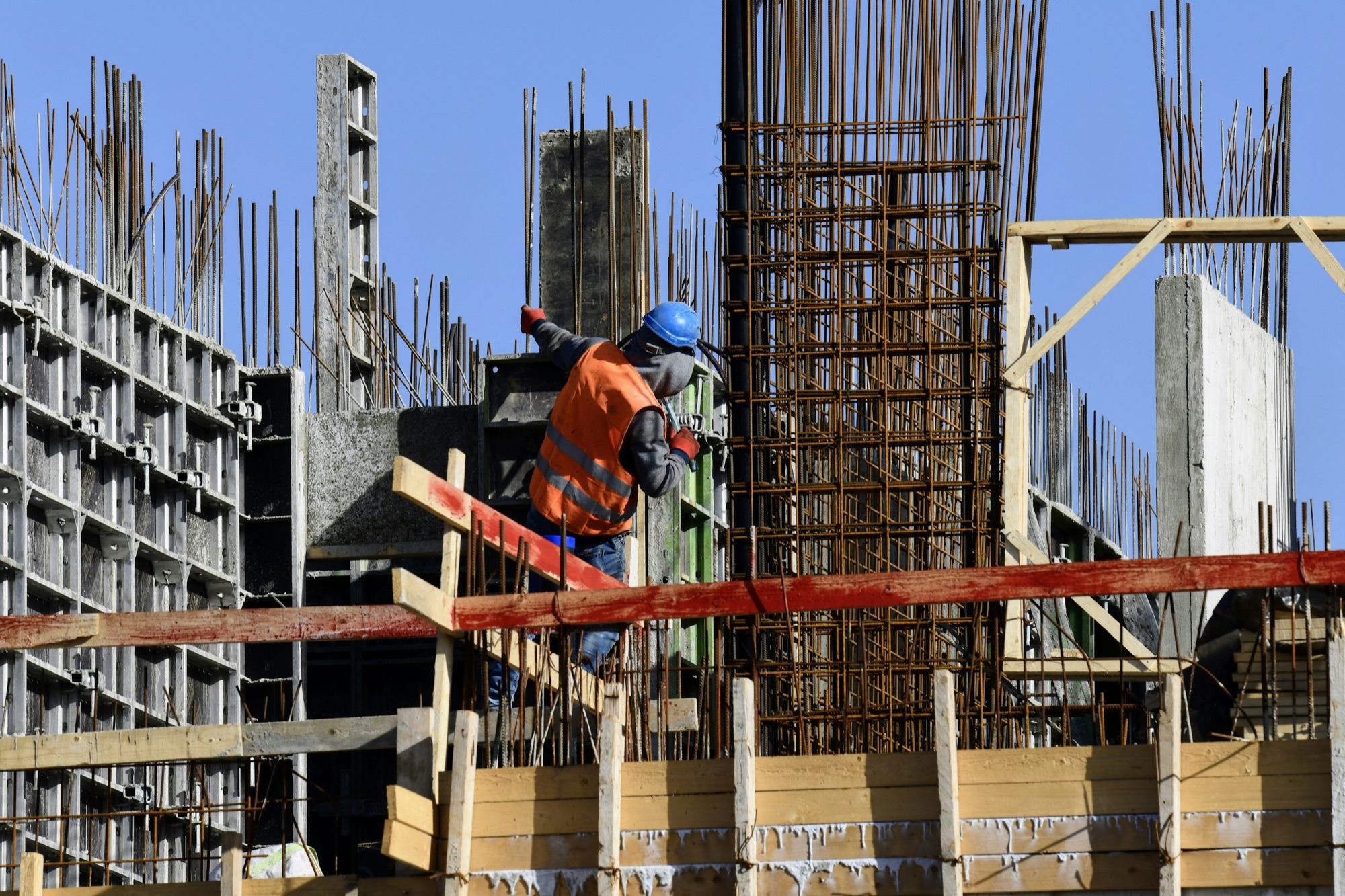 A worker on formwork beside a tall column of rebar