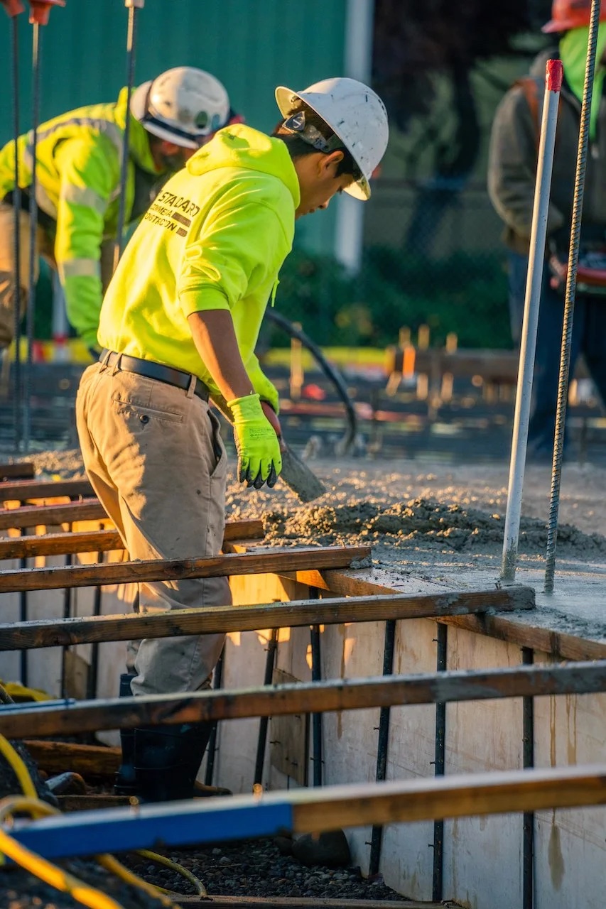 A field lead in a yellow hoodie working a concrete pour beside wood forms