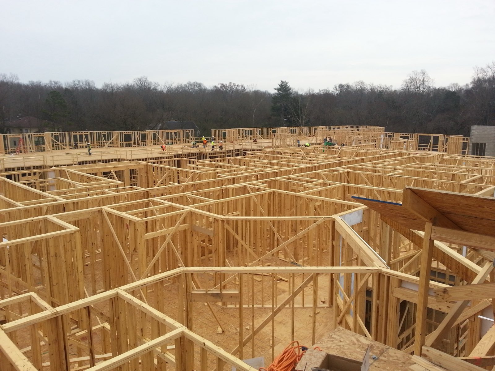 Several carpenters in high-visibility vests working across an open wood floor frame