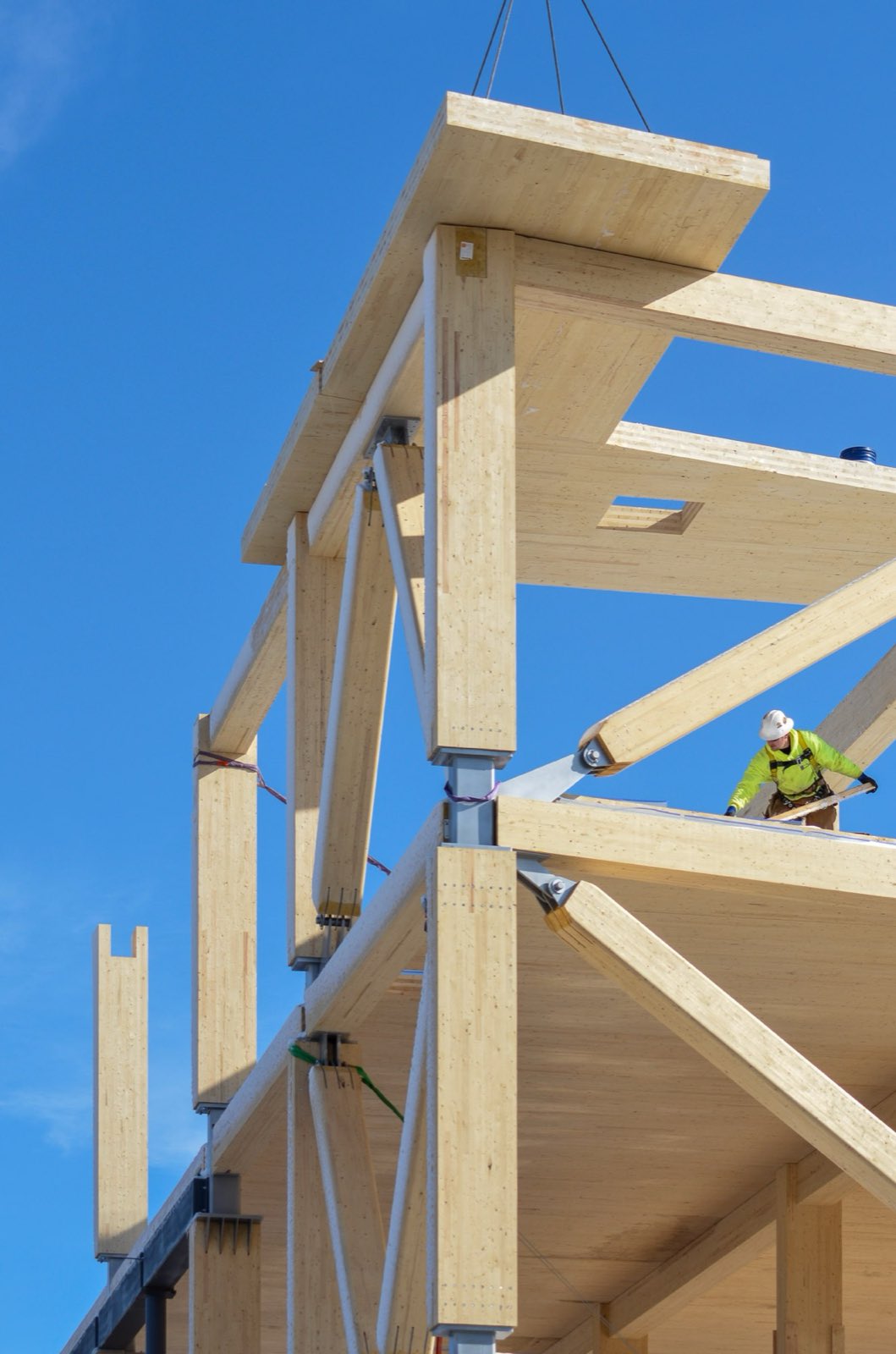 A carpenter on a mass-timber frame against a clear sky