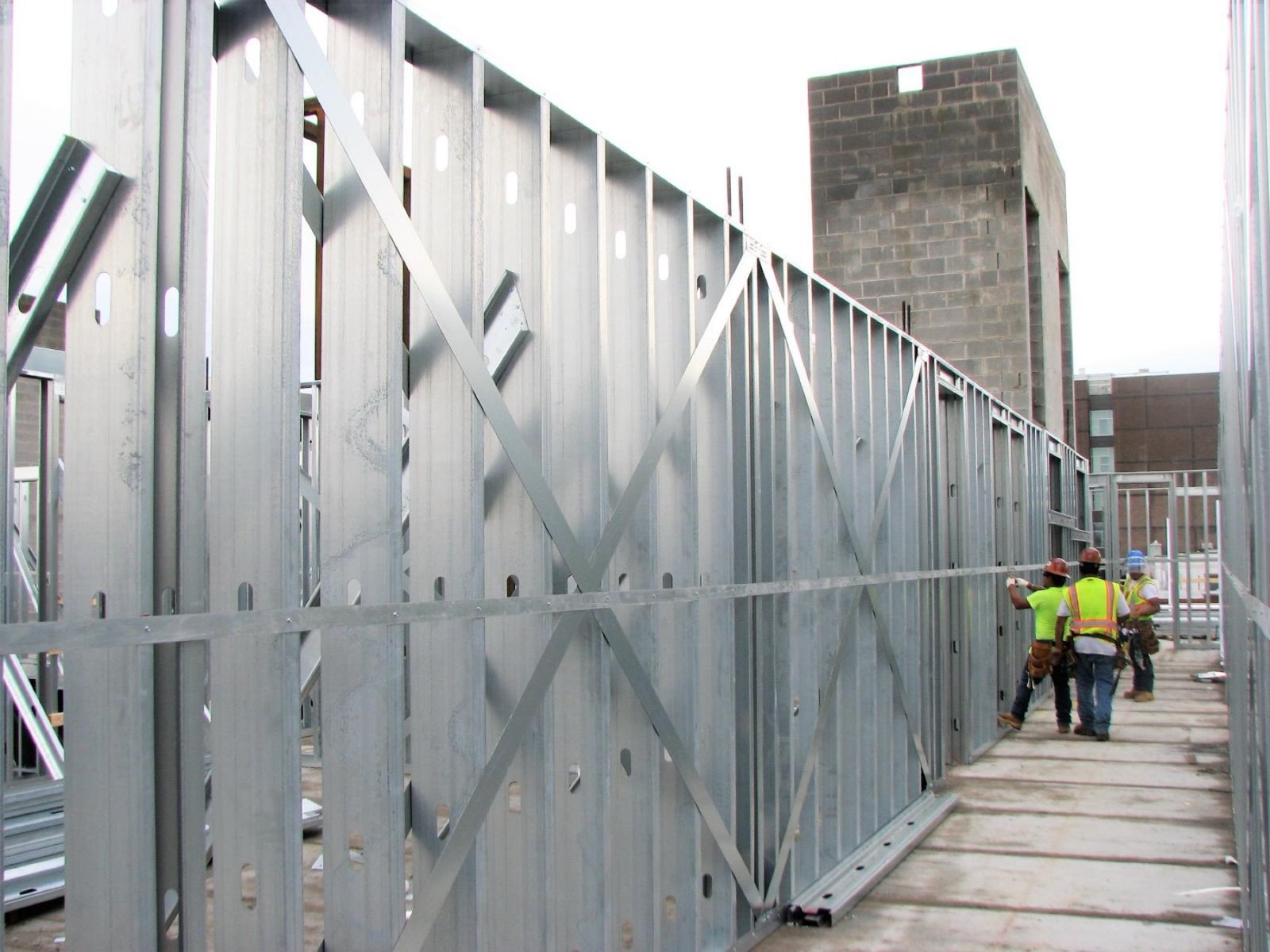 Three workers walking a metal stud wall on an upper floor