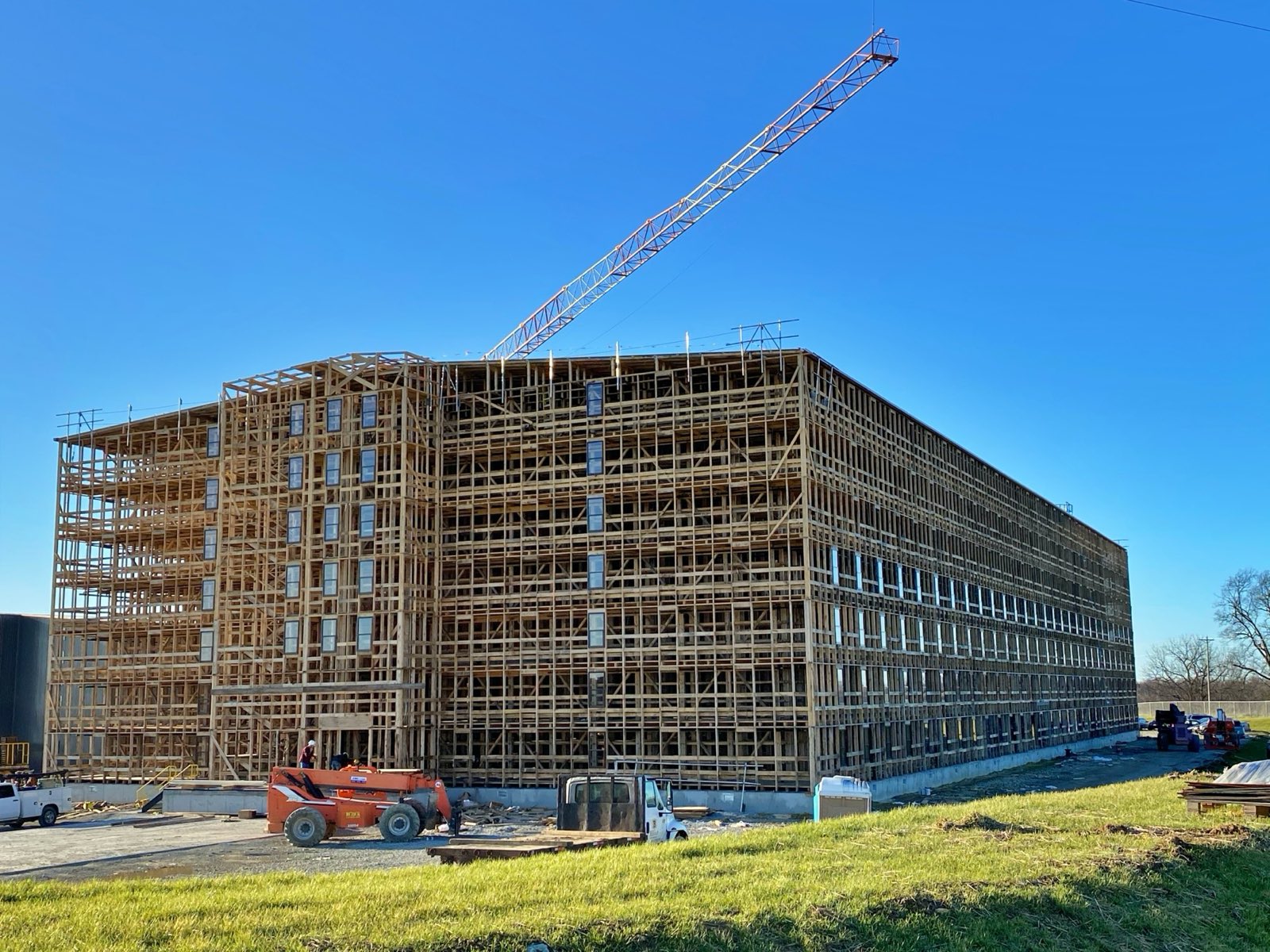 A long multi-story wood-framed building under construction with a tower crane against a clear sky